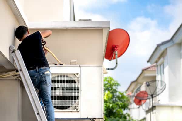 Person working on an outdoor AC unit on a sunny day.