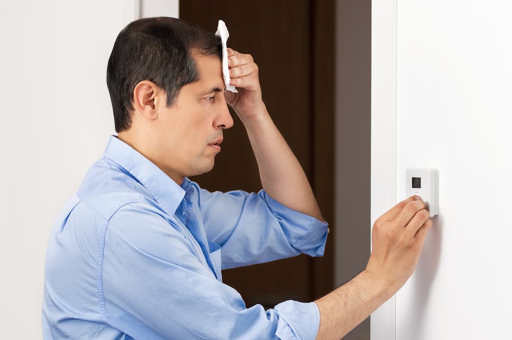 Man turning down heat on the AC system as it is seems to be hot in his home.