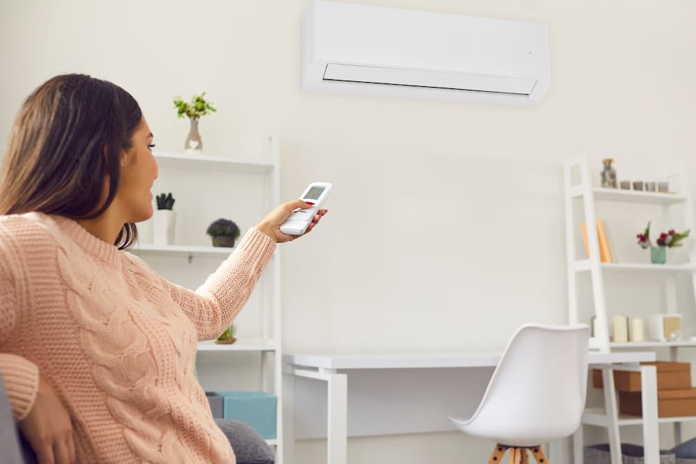 Woman controlling the temperature of her indoor AC unit with a remote.
