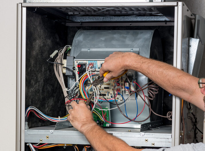 Person cutting wires on a circuit board within an HVAC unit